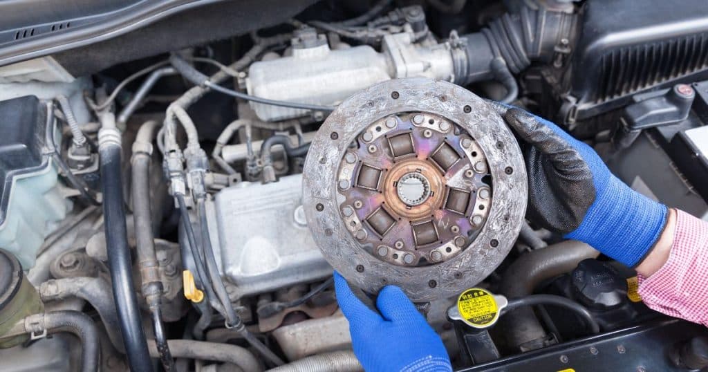 Person in blue gloves holding a clutch above an engine