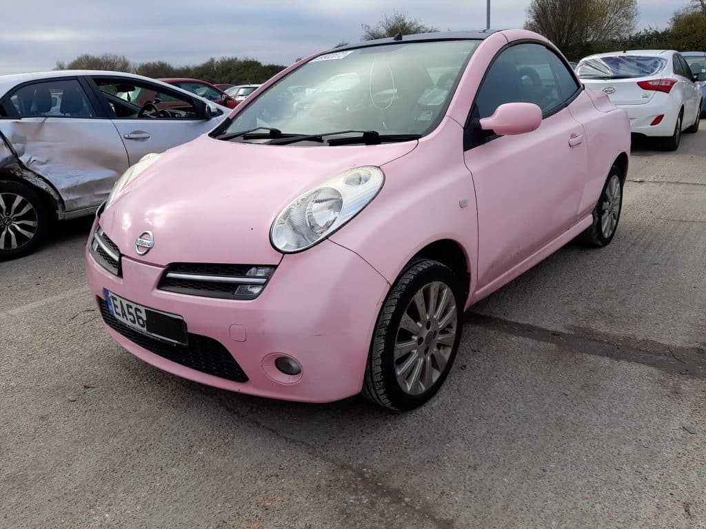 A side view of a parked pink Nissan Micra